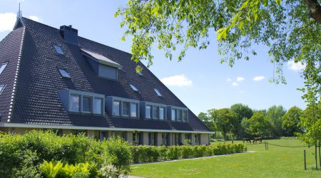 Modern zorgboerderij gebouw met groen dak omgeven door tuin en gras voor ouderenzorg en dementiezorg